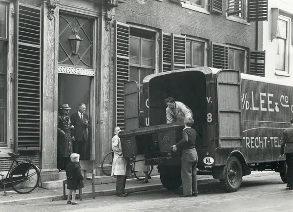 Zwart-witfoto van verhuizers van C.A. van der Lee & Co die een groot eikenhouten meubel in hun verhuiswagen tillen, Minrebroederstraat in Utrecht, 1945 tot 1955. Een ander verhuisfirma, niet De Bresser.