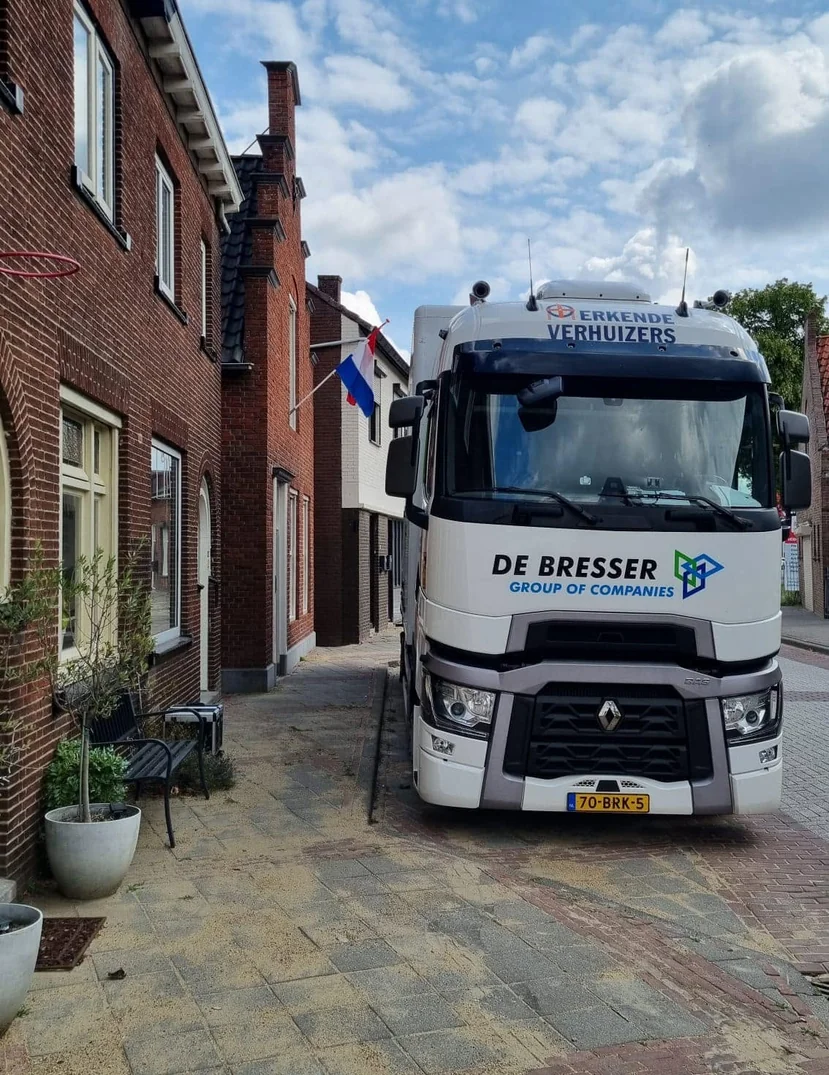 Vrachtwagen van De Bresser in een smalle straat met bakstenen huizen en een Nederlandse vlag