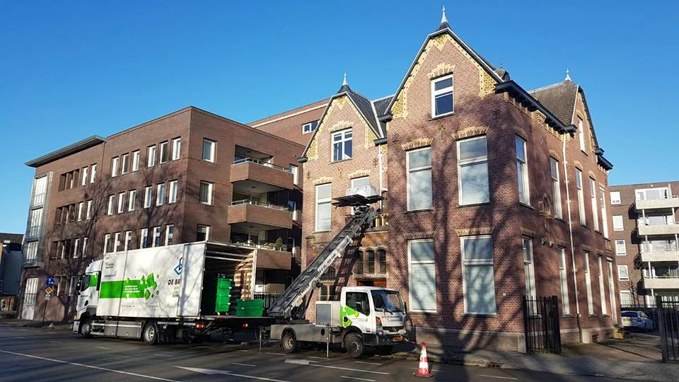 Verhuislift tegen een appartementengebouw, met verhuiswagens ervoor