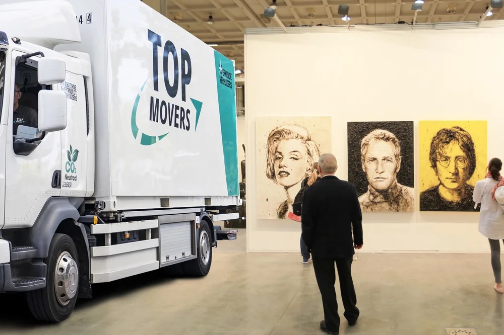 Verhuiswagen van Top Movers in een expositiehal met geschilderde portretten aan de wand
