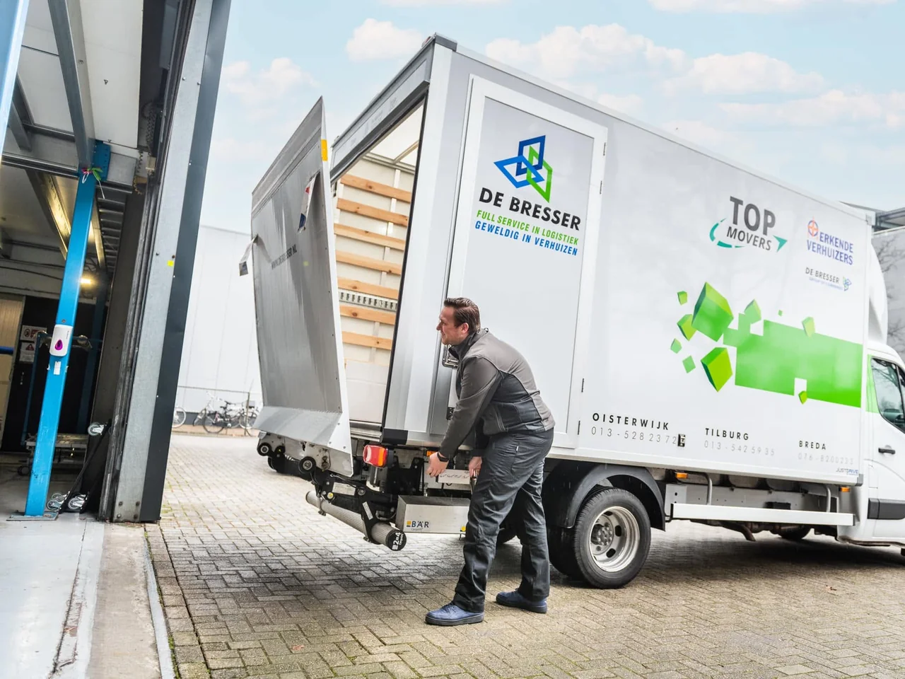 Verhuizer van De Bresser bij de laadklep van een eigen vrachtwagen met open zijdeur