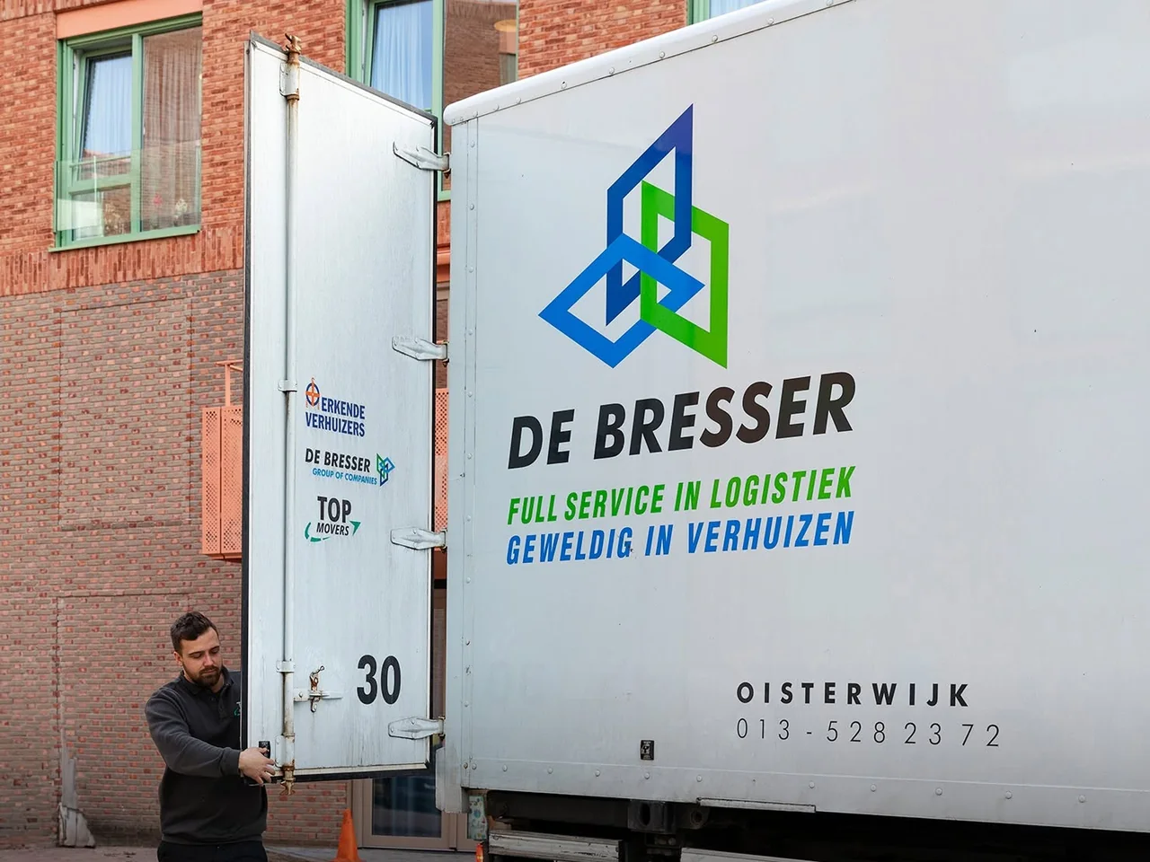 Medewerker van De Bresser opent de achterdeur van een eigen vrachtwagen met de opdruk full service in logistiek