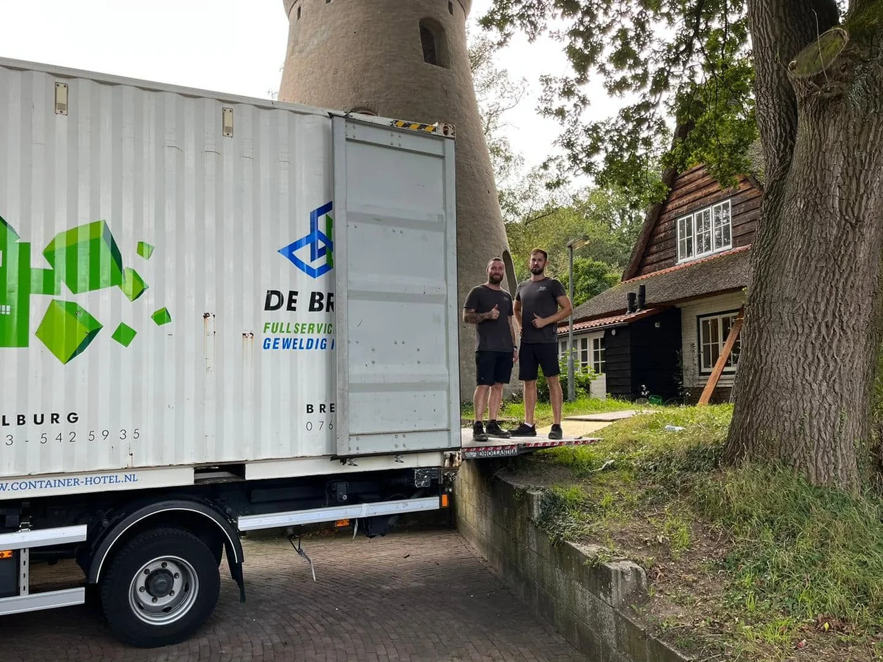 Containerwagen van De Bresser bij een molen, met twee medewerkers naast de opslagcontainer