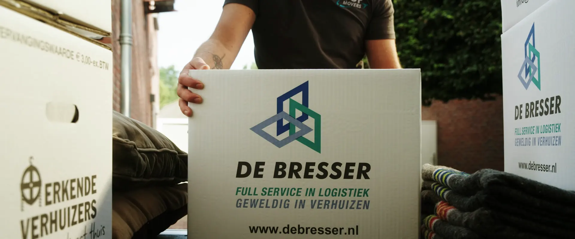 Verhuizer met een verhuisdoos van De Bresser, tussen gestapelde dozen en verhuisdekens