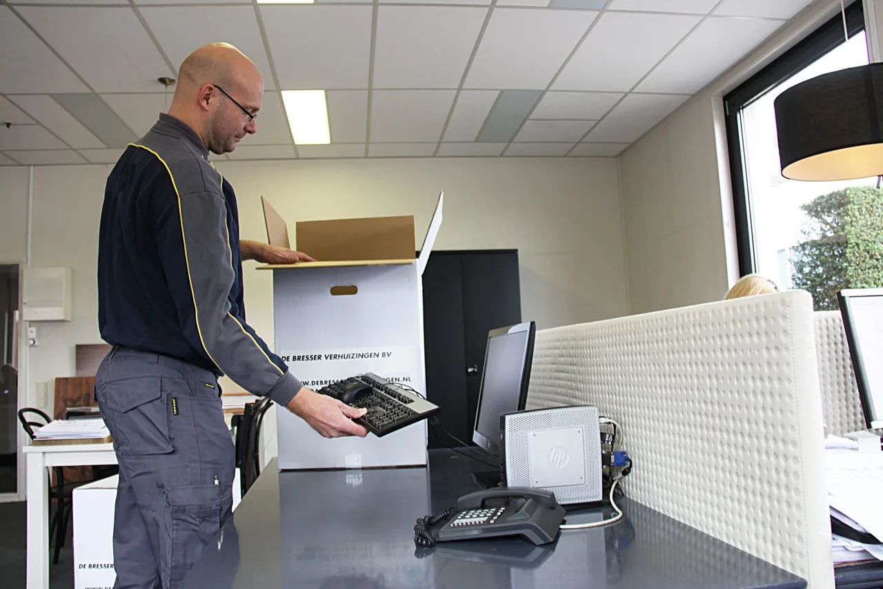Medewerker pakt een toetsenbord uit een verhuisdoos op een kantoorbureau