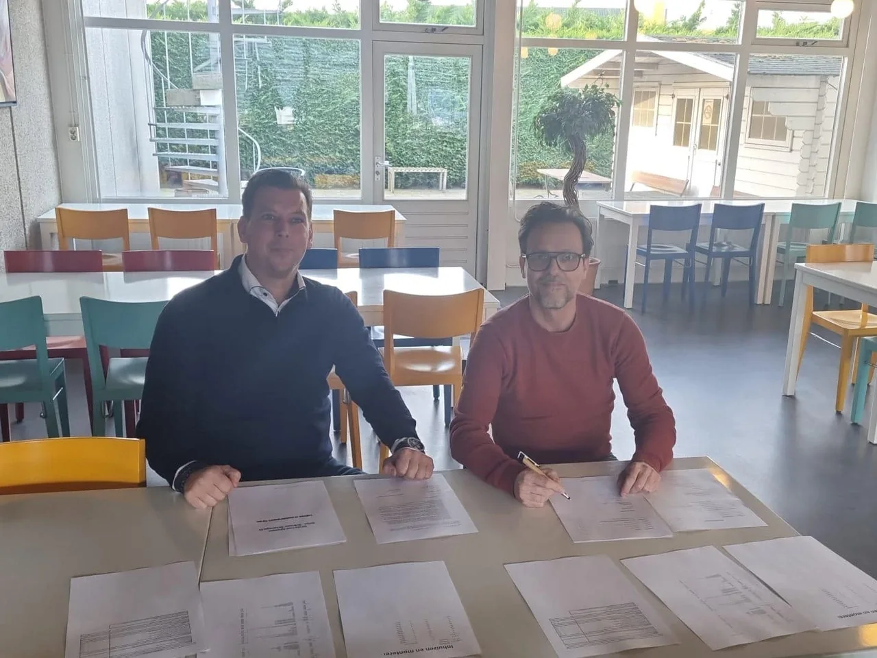 Twee mannen tekenen samen een overeenkomst aan een tafel met papieren