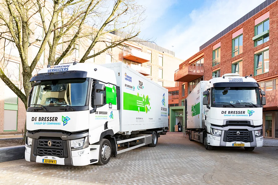 Twee vrachtwagens van De Bresser op een binnenplaats tussen nieuwbouwappartementen