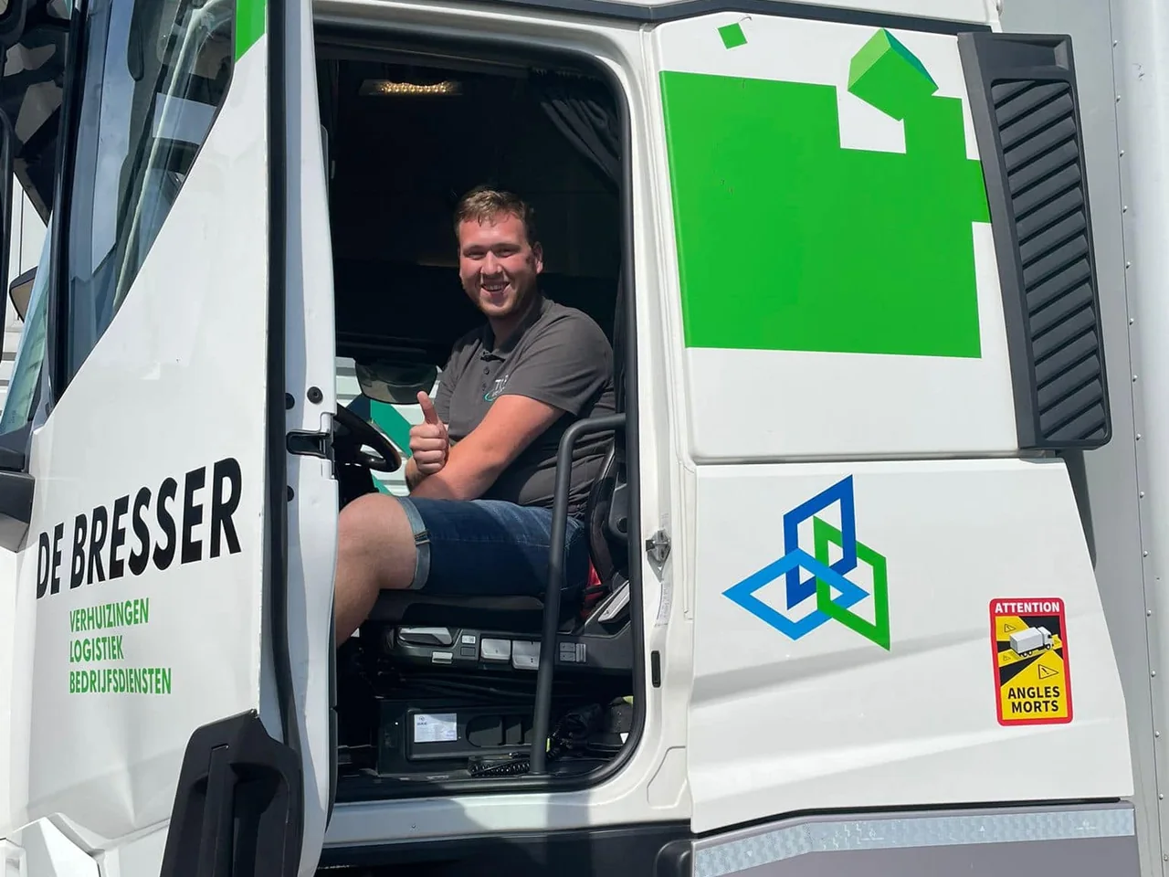 Chauffeur steekt zijn duim op vanuit de open cabine van een witte vrachtwagen van De Bresser